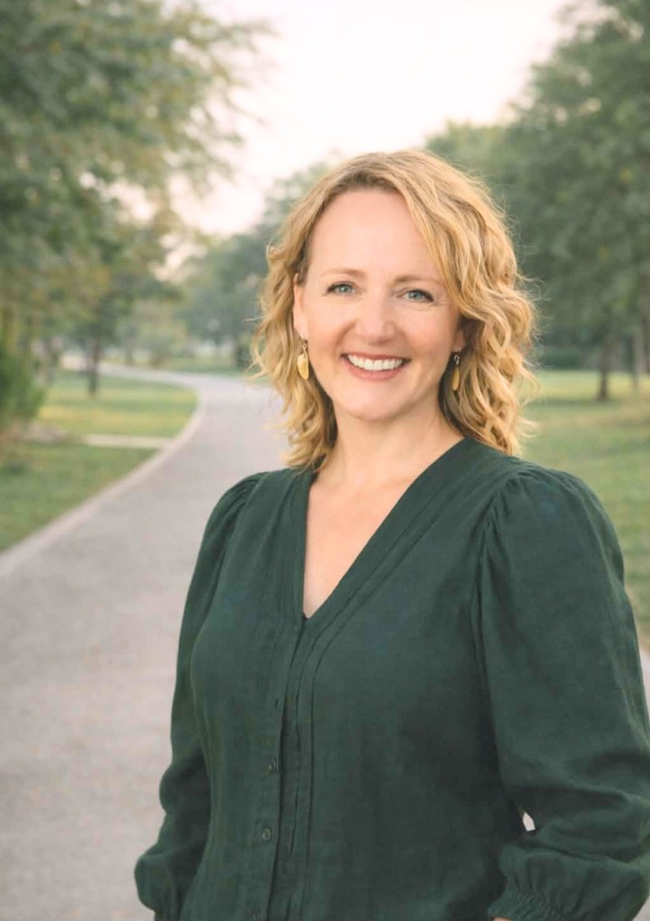 Professional portrait of Leigh Spencer, writer and guide, smiling outdoors in a park setting.
